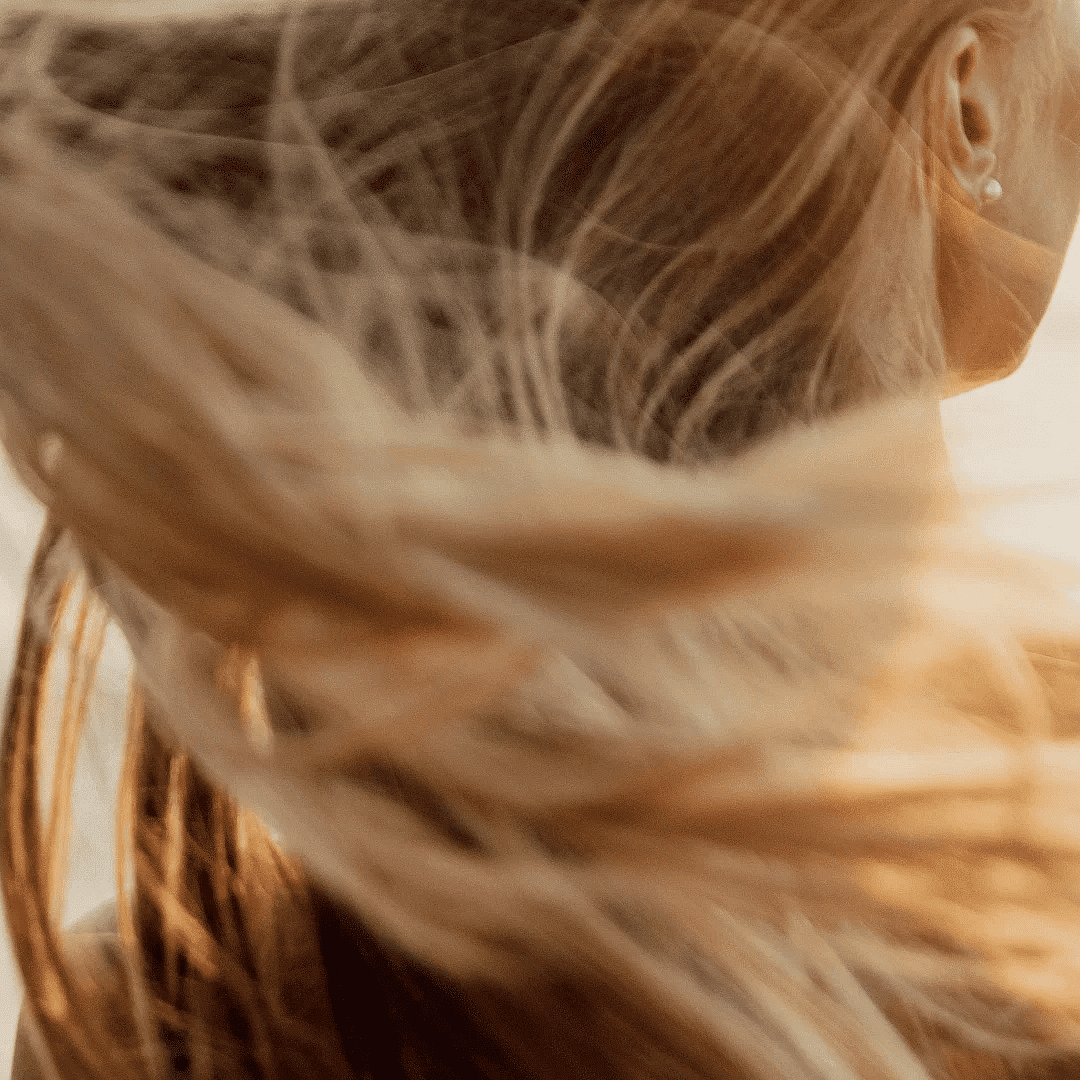 A person with long blonde hair blowing in the wind, facing the ocean at sunset.