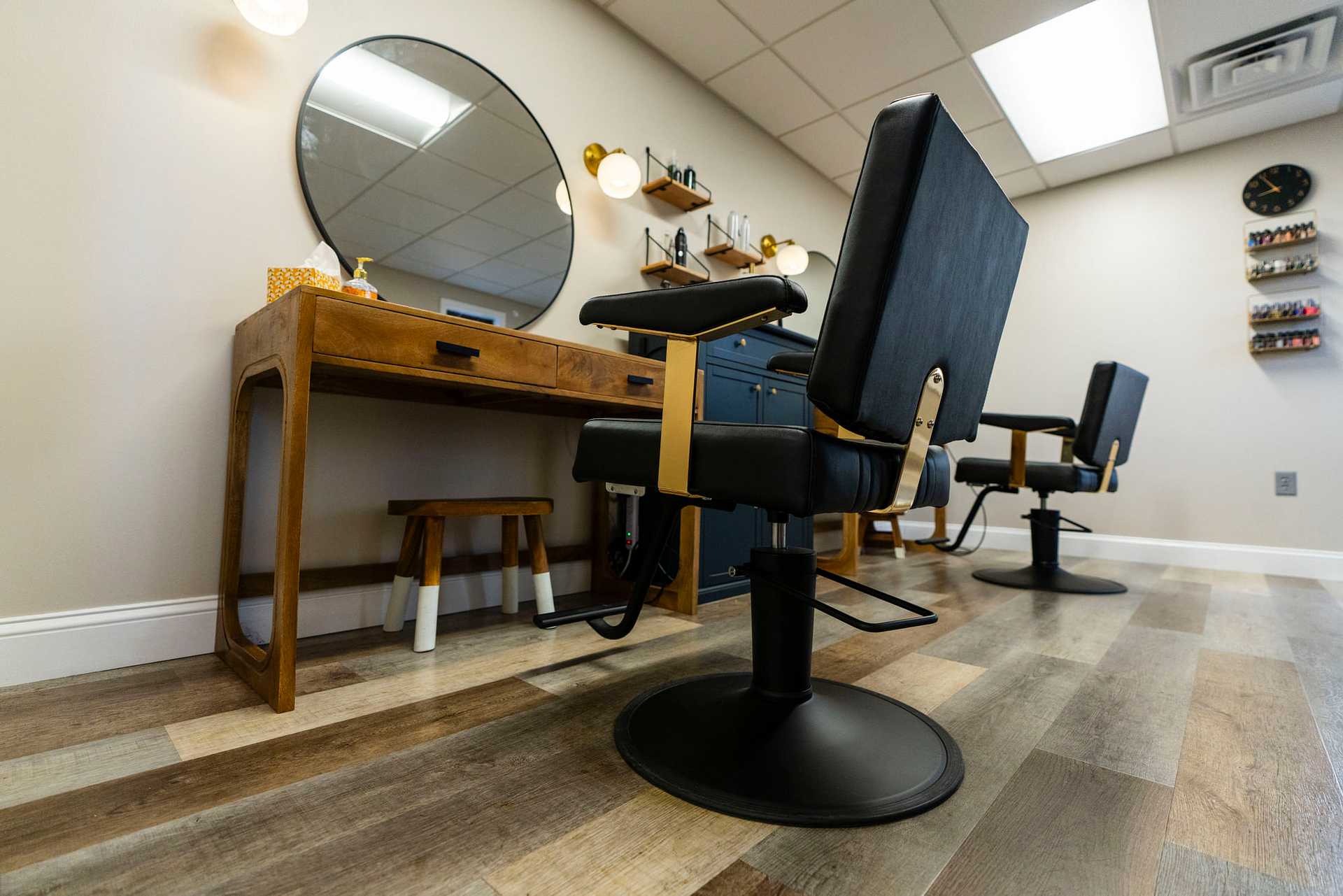 Modern barbershop with wooden furniture, round mirror, and black chairs on a patterned floor.